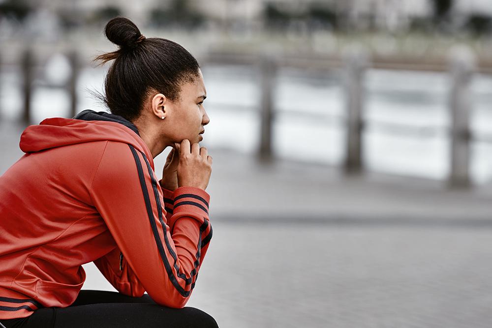 Young black woman wearing jogging clothes sitting and looking contemplative.