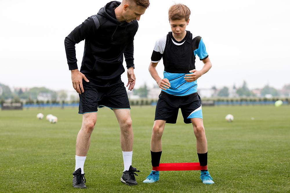 Male coach helping young male soccer athlete.
