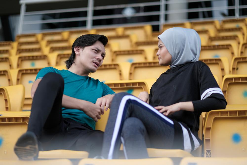 Young man talking to young woman in head scarf in a sports stadium.