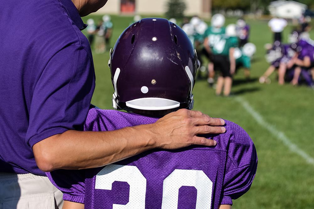 Young football player with coach by his side.