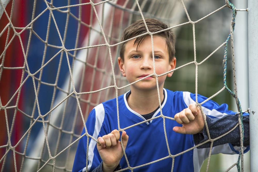 Young boy looking out through soccer net.