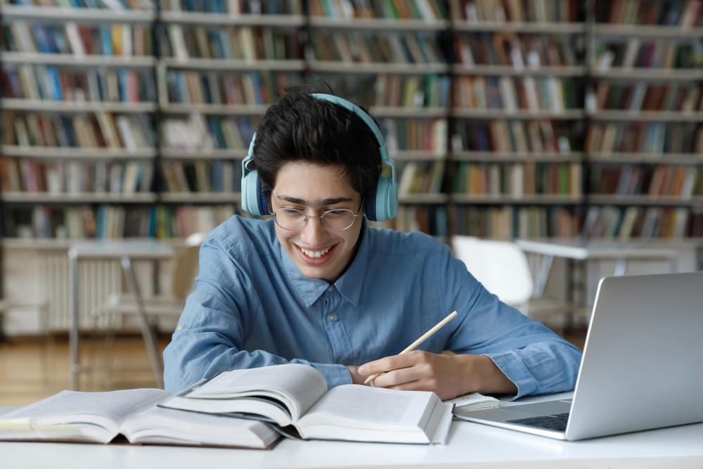 Teen boy smiling while doing schoolwork and wearing headphones.