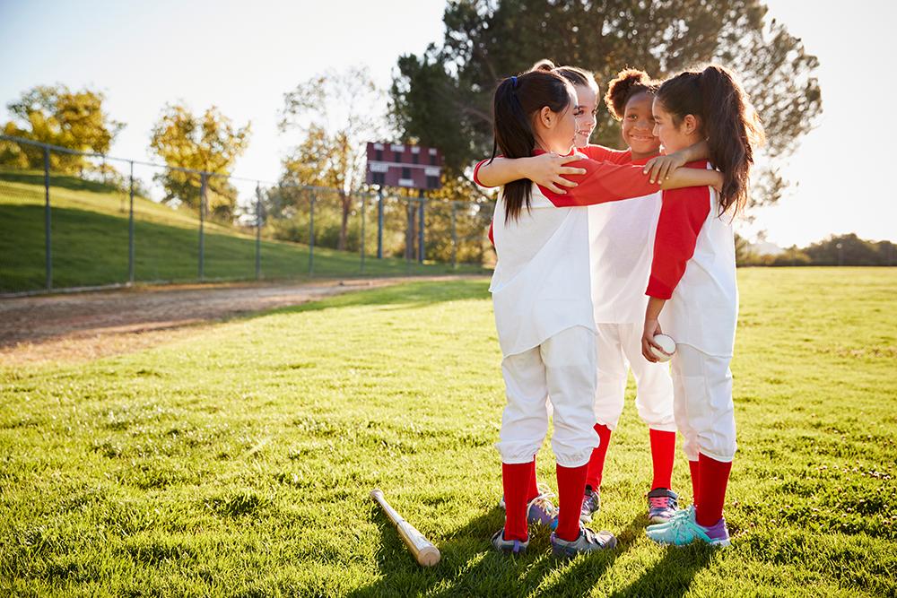 Diverse young girls in a huddle on softball field.